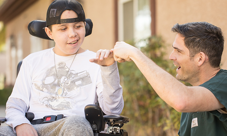 Male teenage patient in wheelchair laughing with male employee