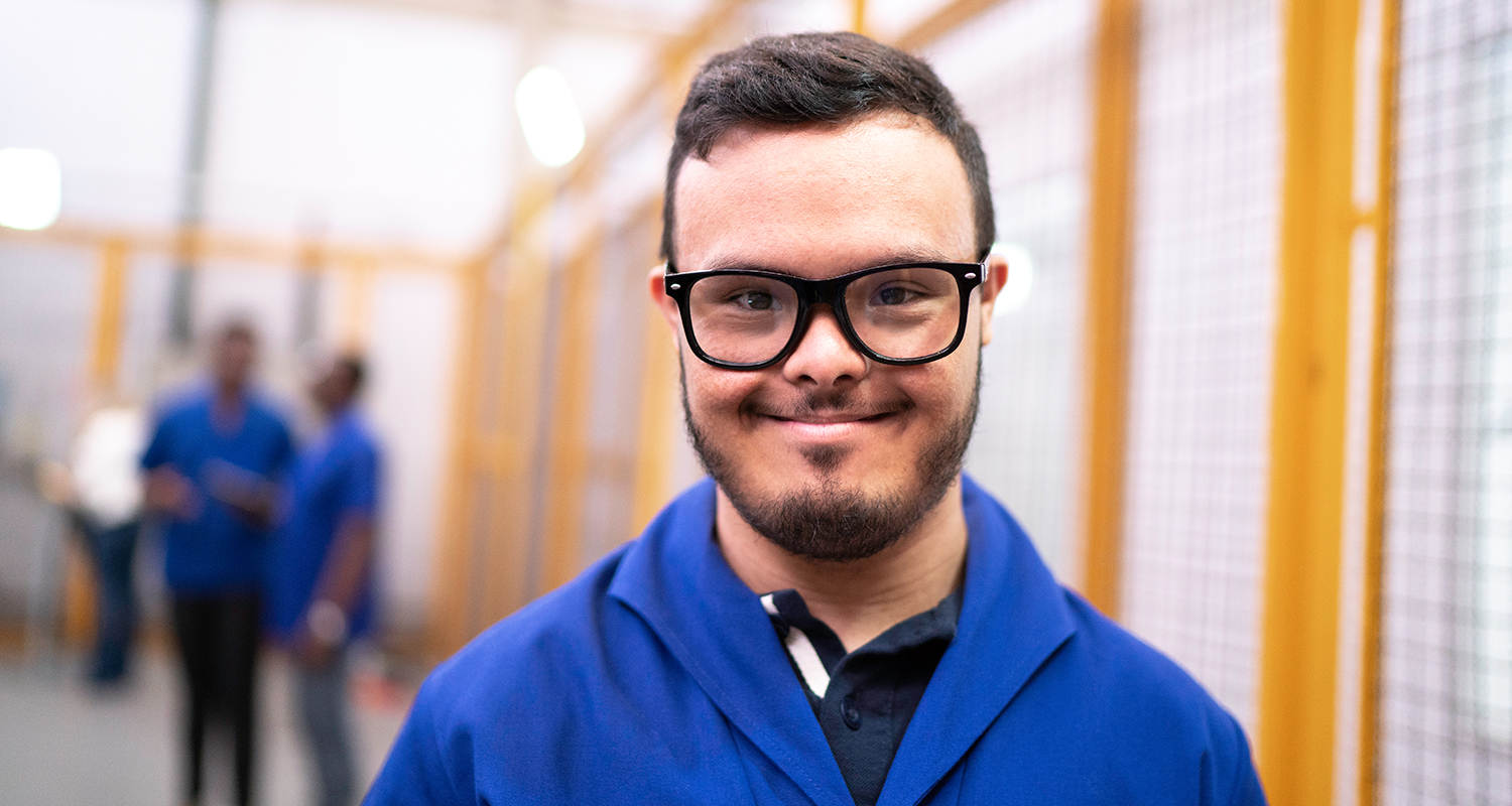 Closeup of young man with Down Syndrome smiling at the camera at his workplace