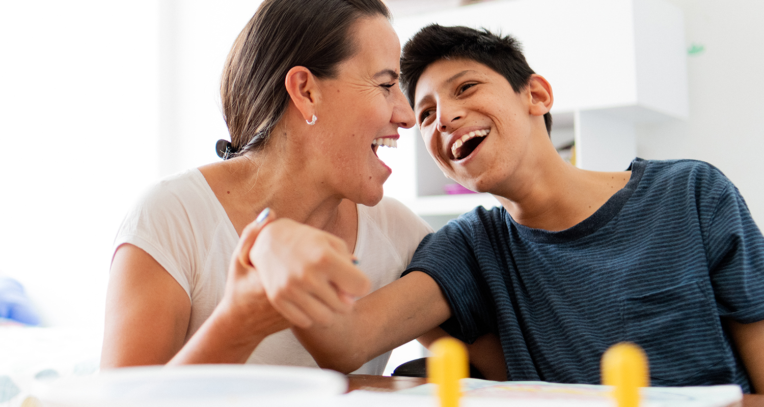 boy with autism laughing with mother at table