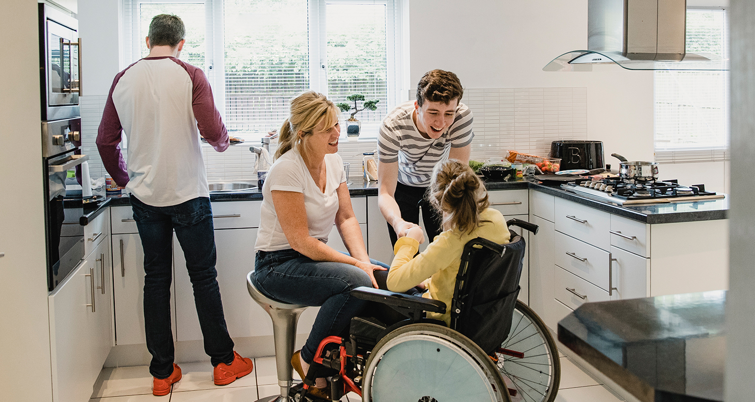 Teenage girl in a wheelchair in kitchen with her parents and brother
