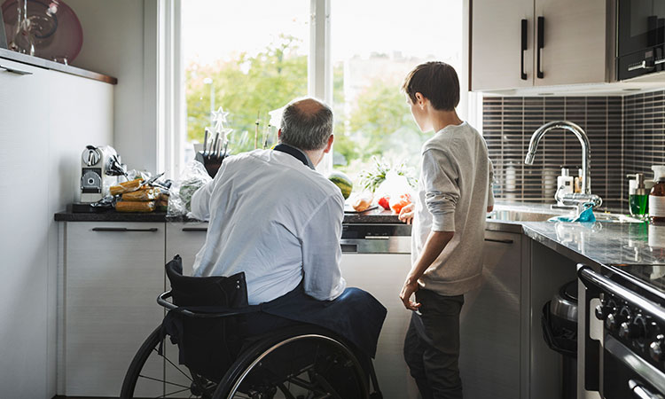 Caucasian father in wheelchair looking out kitchen window with teenage son