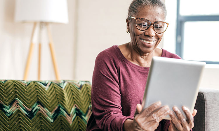 Senior woman looking at tablet while sitting on couch and smiling