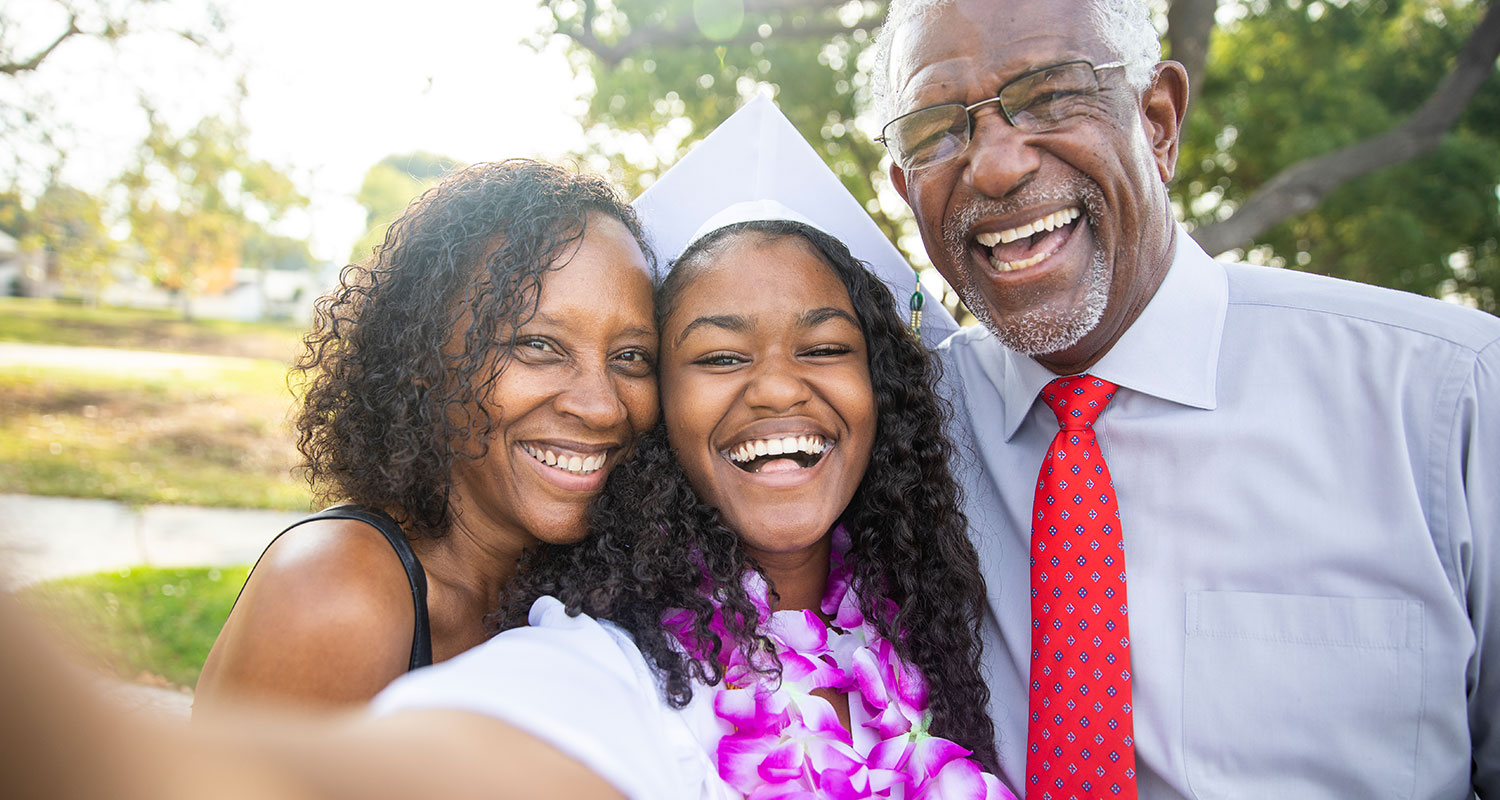 Black family with daughter in graduation hat taking a selfie and smiling
