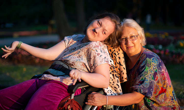 Young woman sitting in wheelchair with female caregiver sitting next to her