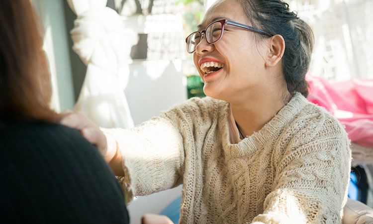 woman of asian descent smiling and laughing while talking to a friend in her home
