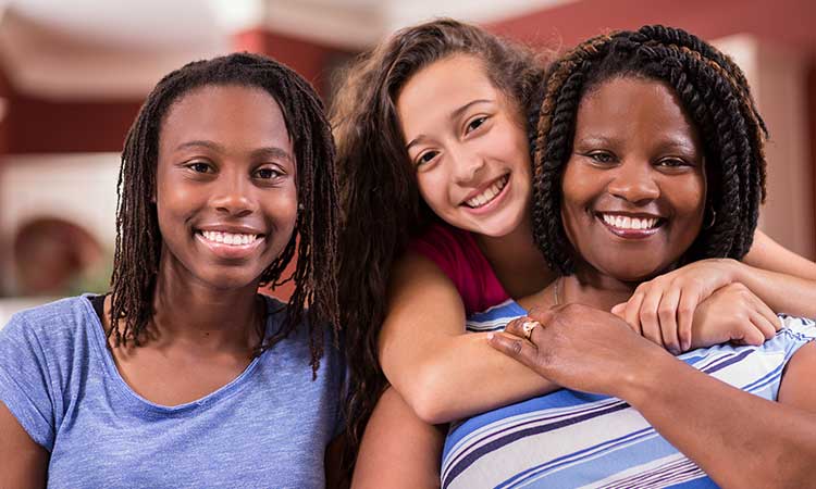 Foster mother and two teen girls hugging and smiling