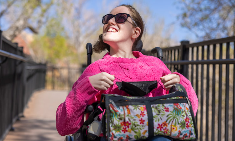 young woman with disabilities in wheelchair with hot pink sweater on and carrying a bag