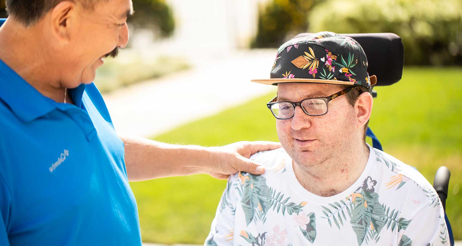 Male rehabilitation patient in wheelchair with male caregiver touching his shoulder
