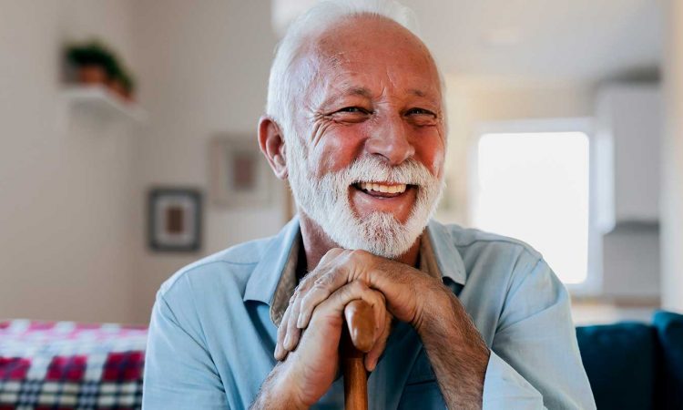 Elderly man with white beard smiling on couch at home