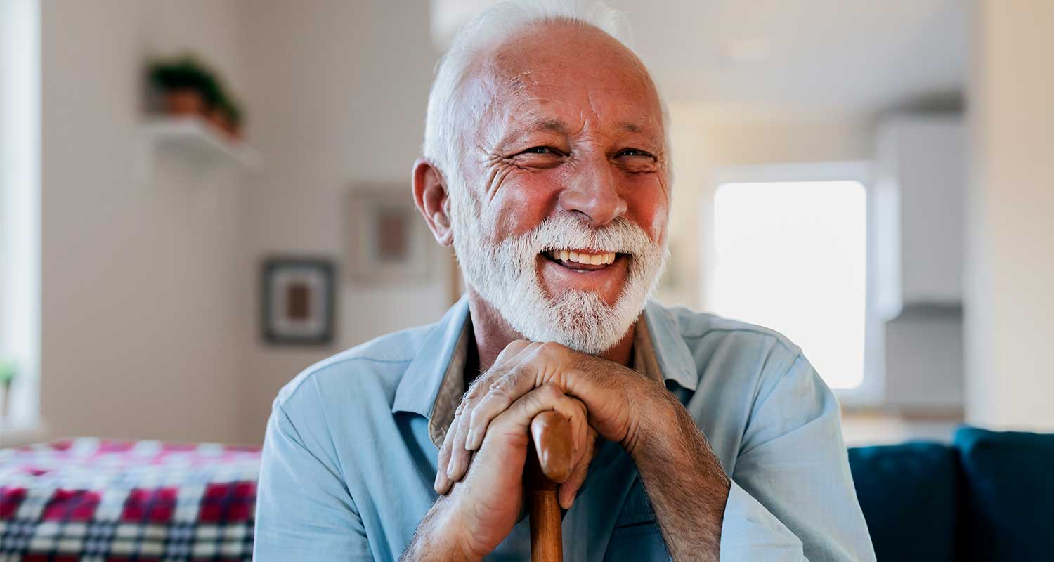Elderly man with white beard smiling on couch at home