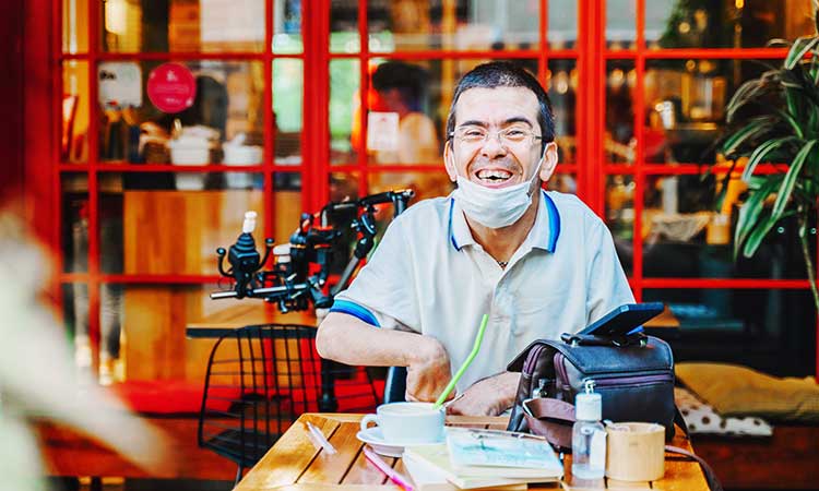 Man with developmental disability having coffee on a restaurant patio and smiling at the camera