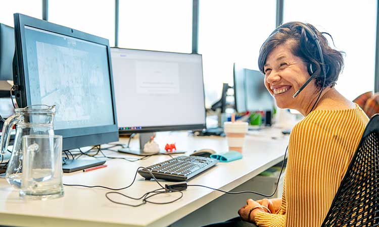 Woman with developmental disability working at her computer at her desk and smiling.