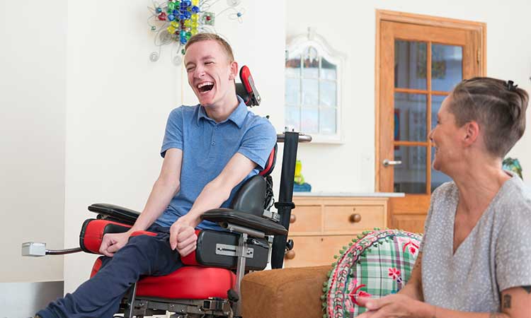 Young man in wheelchair laughing with female caregiver in his home