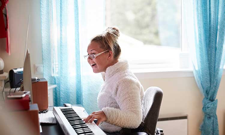 A young blonde-haired woman in a wheelchair is playing piano and smiling