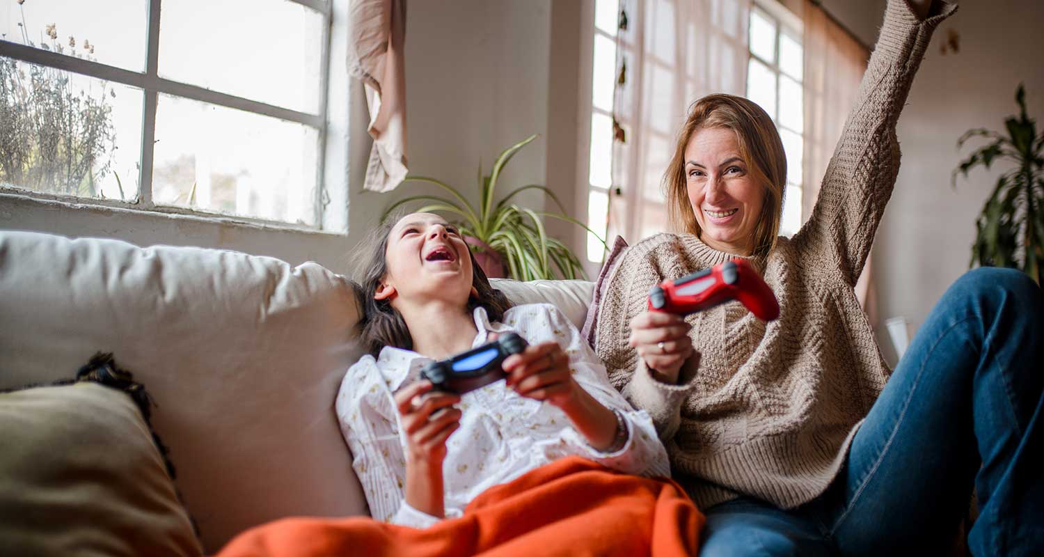 Caucasian mother and teenage daughter playing a video game and laughing on the couch