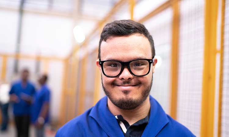 Closeup of young man with Down Syndrome smiling at the camera at his workplace