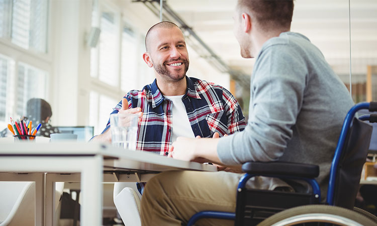 Man in wheelchair working at a desk with his coworker