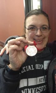 Kari Groebner is a woman wearing a Special Olympics of Minnesota sweatshirt and holding up her Special Olympics medal