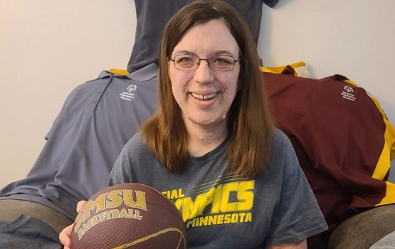 Kari is holding a basketball and showing her collection of Special Olympics t-shirts