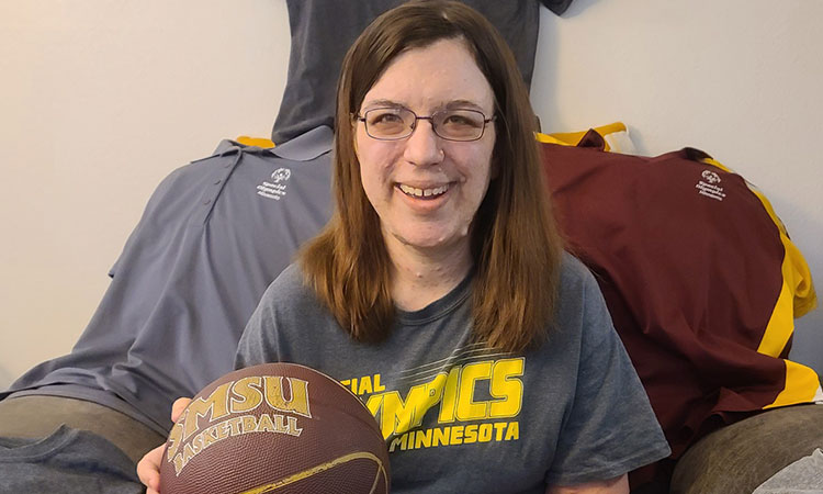 Kari is holding a basketball and showing her collection of Special Olympics t-shirts