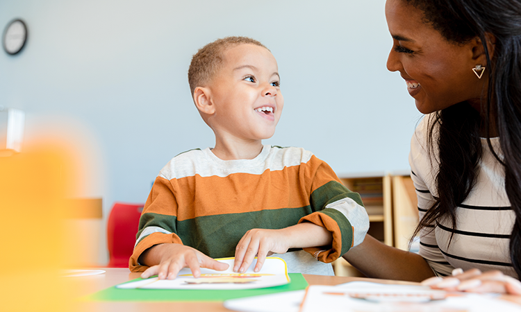 Boy sitting at table with his teacher and smiling