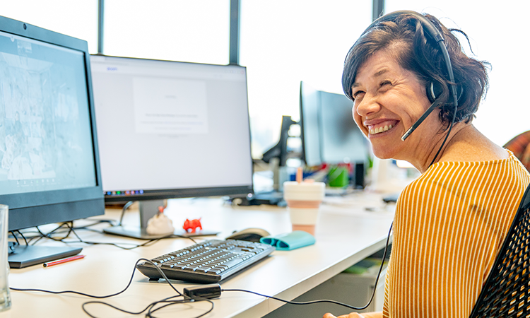 Woman working at computer with headset on and smiling