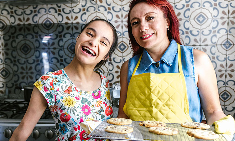 Mom and teenage daughter showing off cookies they baked and smiling