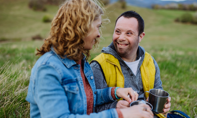 Man and woman sitting in the grass with drinking cups and smiling
