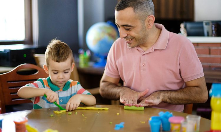 Dad and young son playing with play dough at table