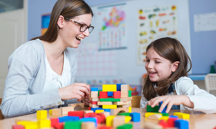 teacher stacking blocks with girl at table